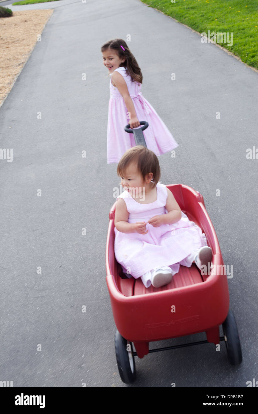Elder sister pulling her younger sister in a red wagon Stock Photo Alamy
