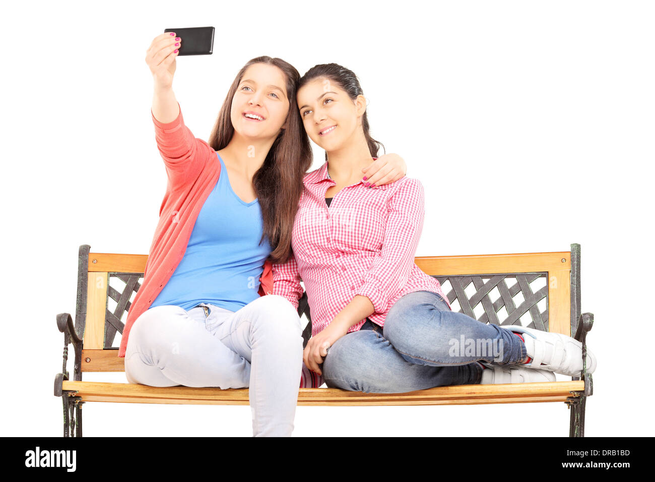Two young girls seated on bench taking picture of themselves with cell phone Stock Photo
