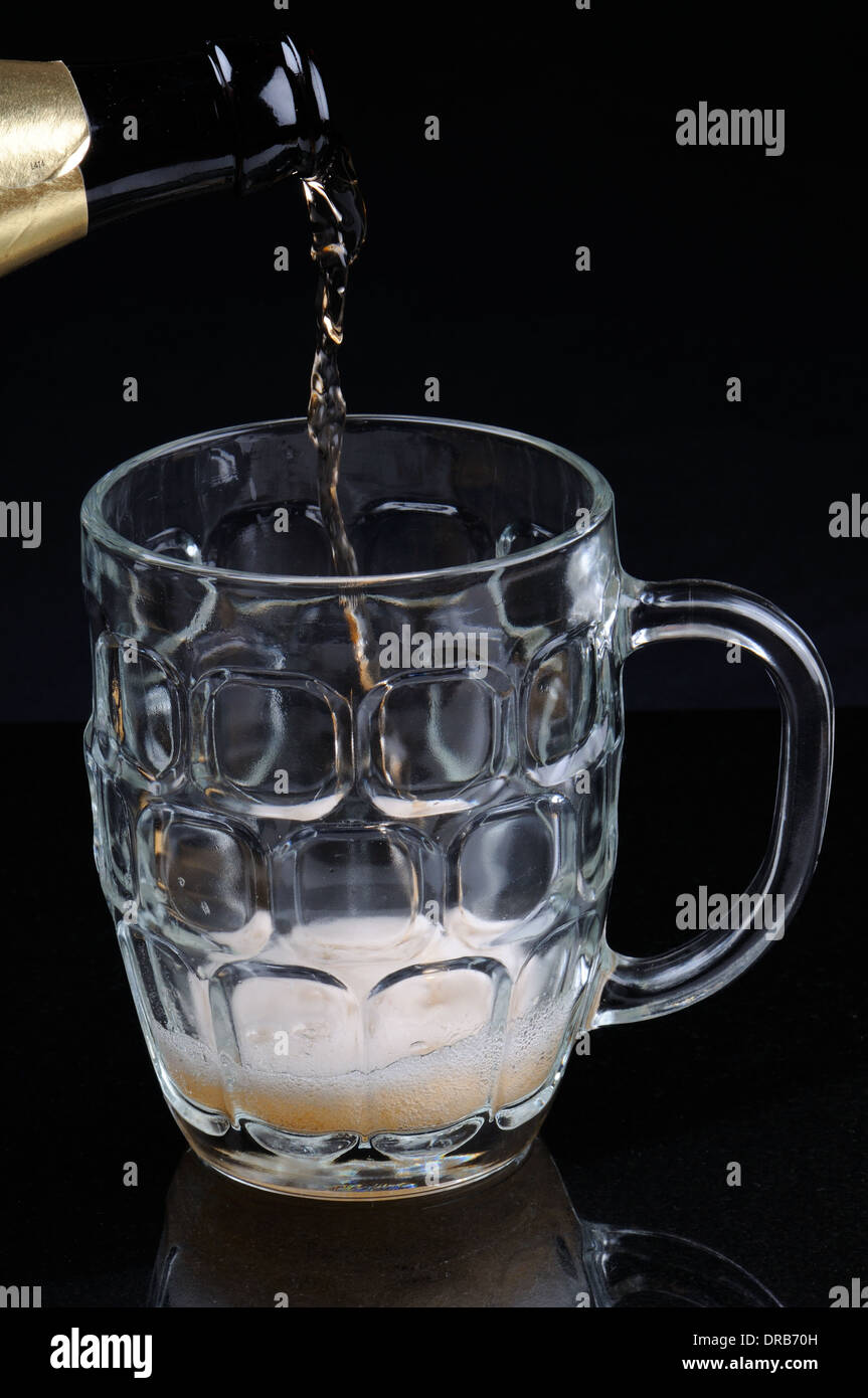 Pouring alcohol from a bottle to a dimpled pint glass Stock Photo