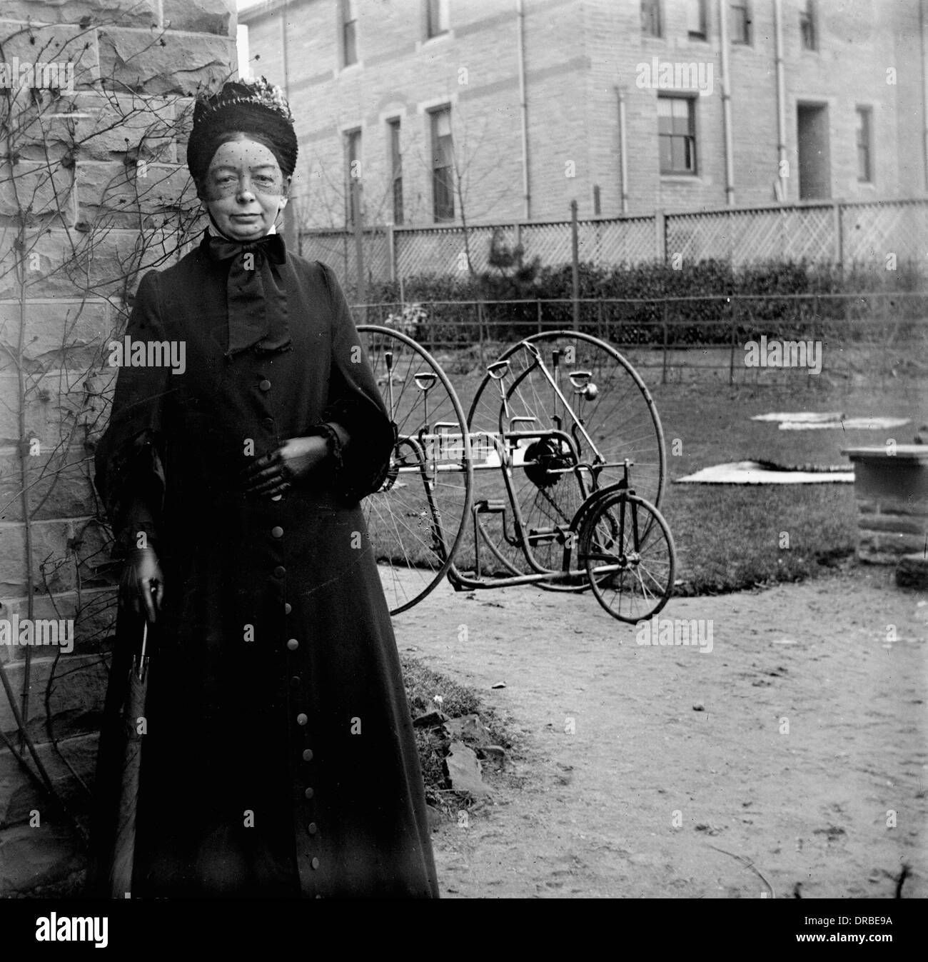 Portrait of a woman in period dress in front of an early two-seat tricycle. Photographed around 1900. Stock Photo