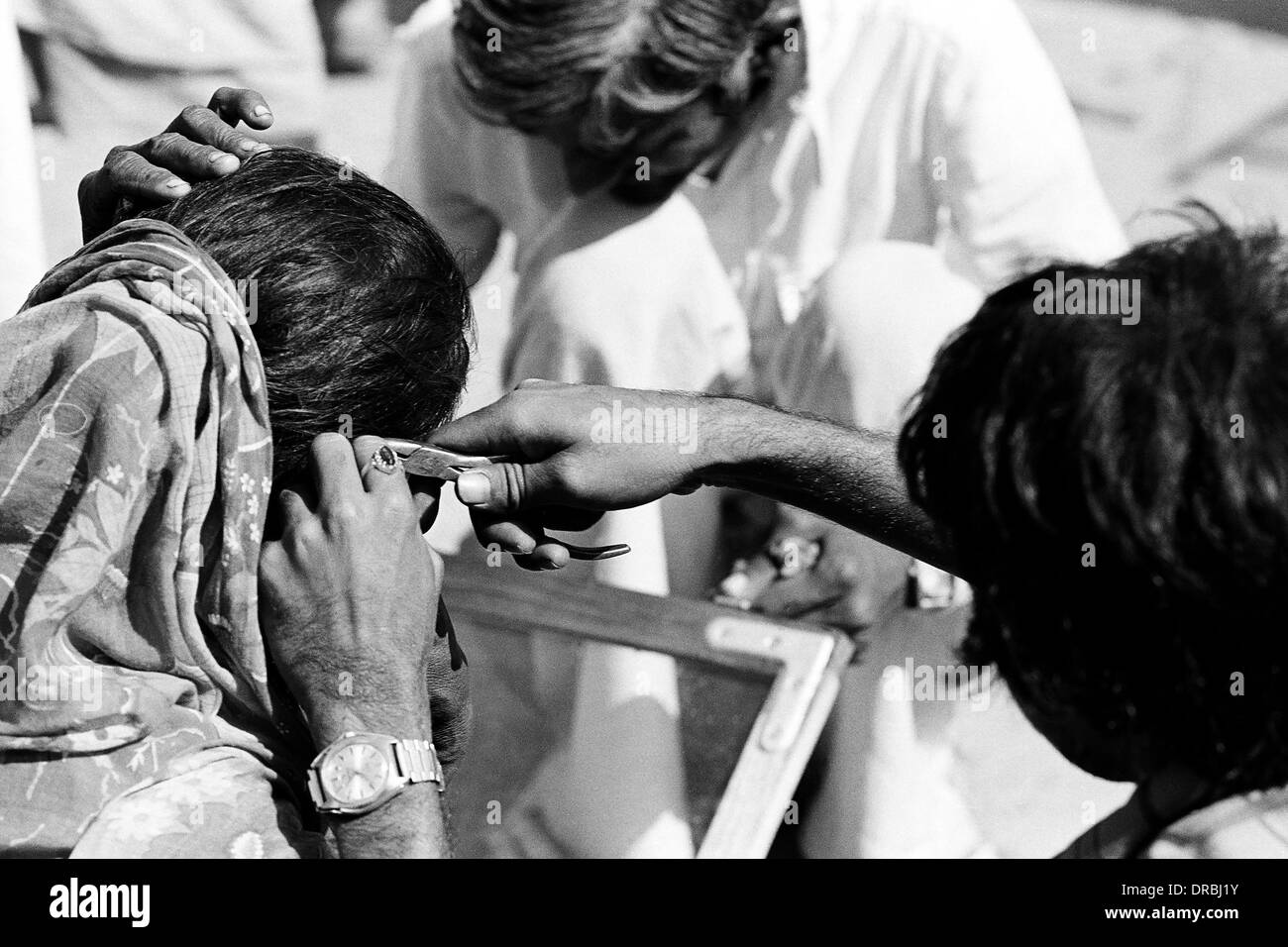 Man fixing woman ear ring with plier, Vautha fair, Gujarat, India, 1983 Stock Photo
