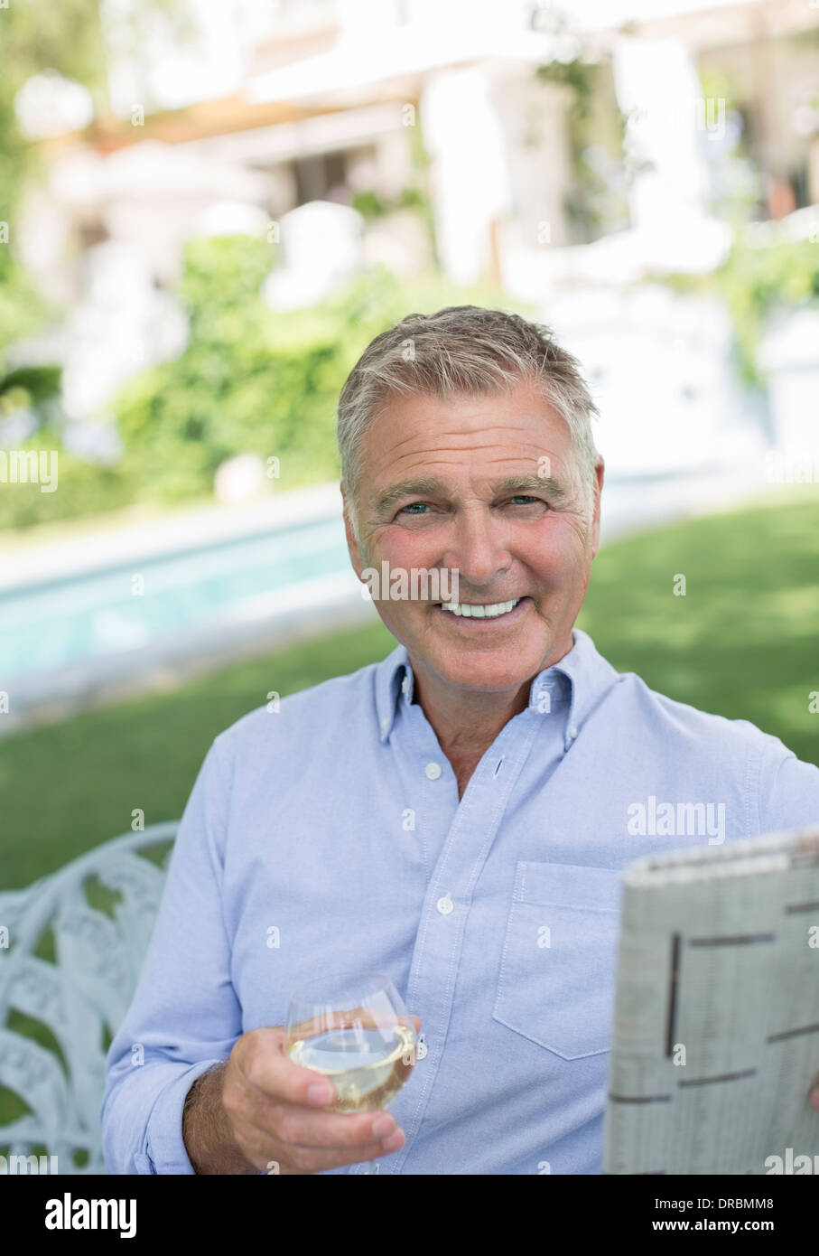 Senior man reading newspaper and drinking wine in backyard Stock Photo