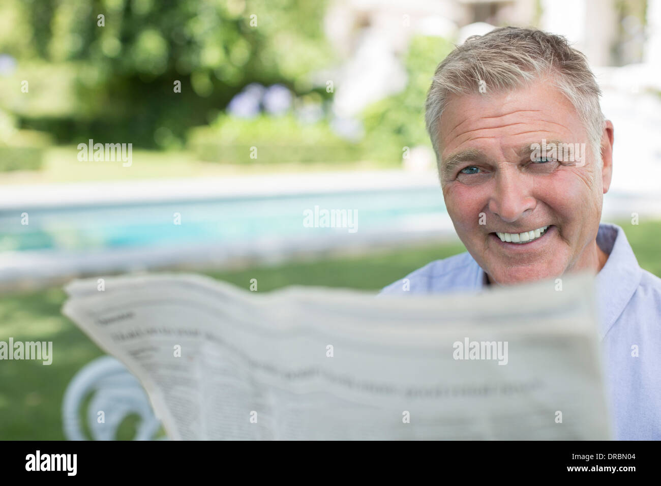 Senior man reading newspaper at poolside Stock Photo