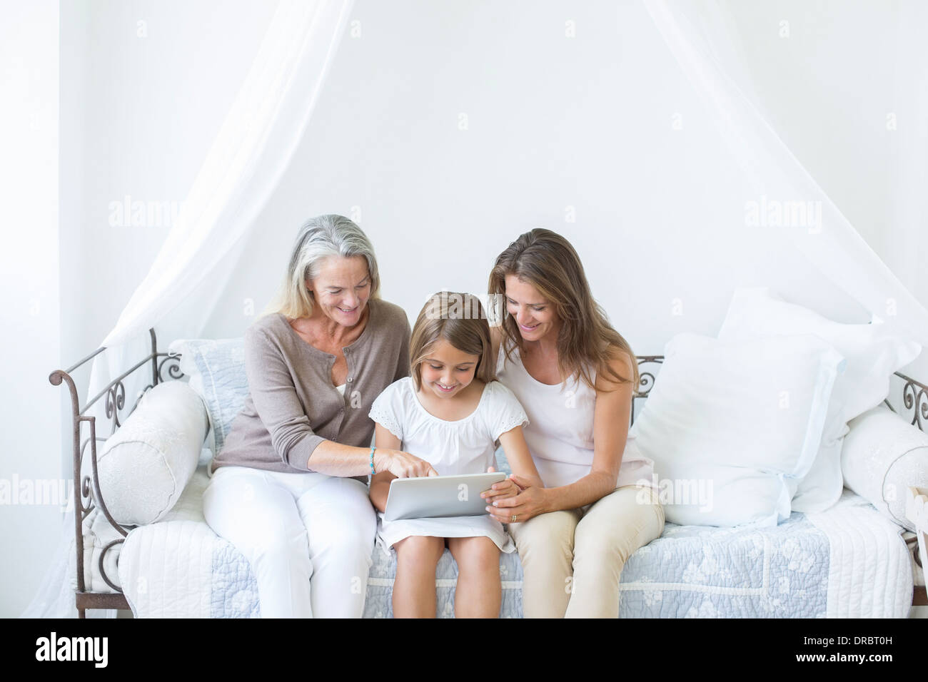 Multi-generation women using digital tablet on daybed Stock Photo