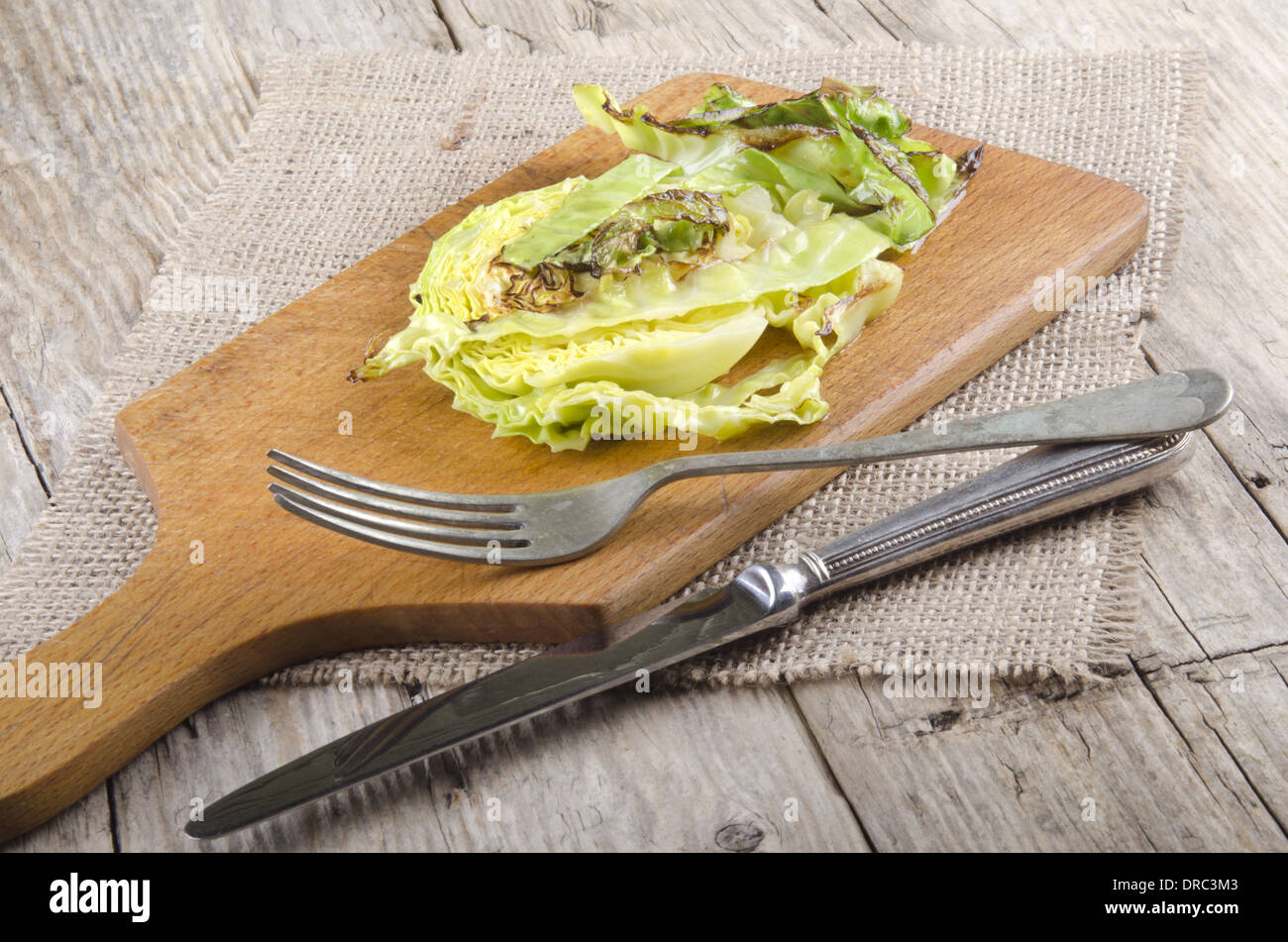 roasted cabbage slice with fork and knife on a wooden board Stock Photo