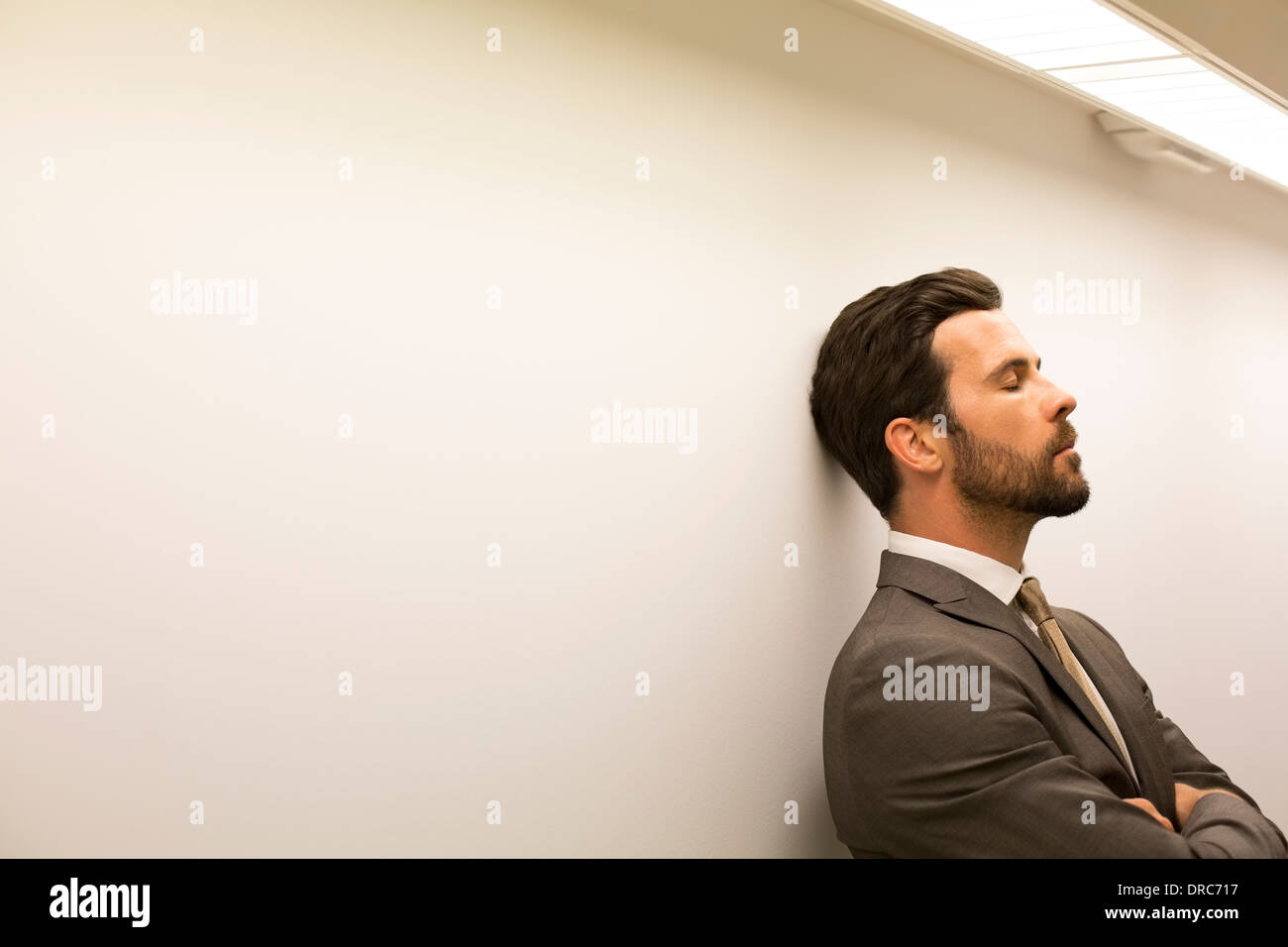 Businessman with eyes closed leaning against wall Stock Photo
