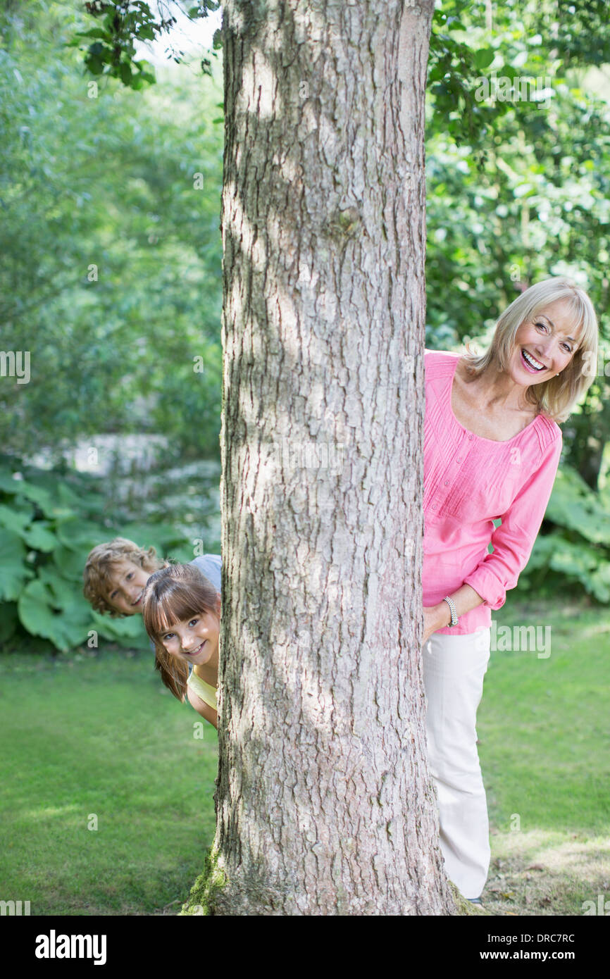 Grandmother and grandchildren peering behind tree Stock Photo