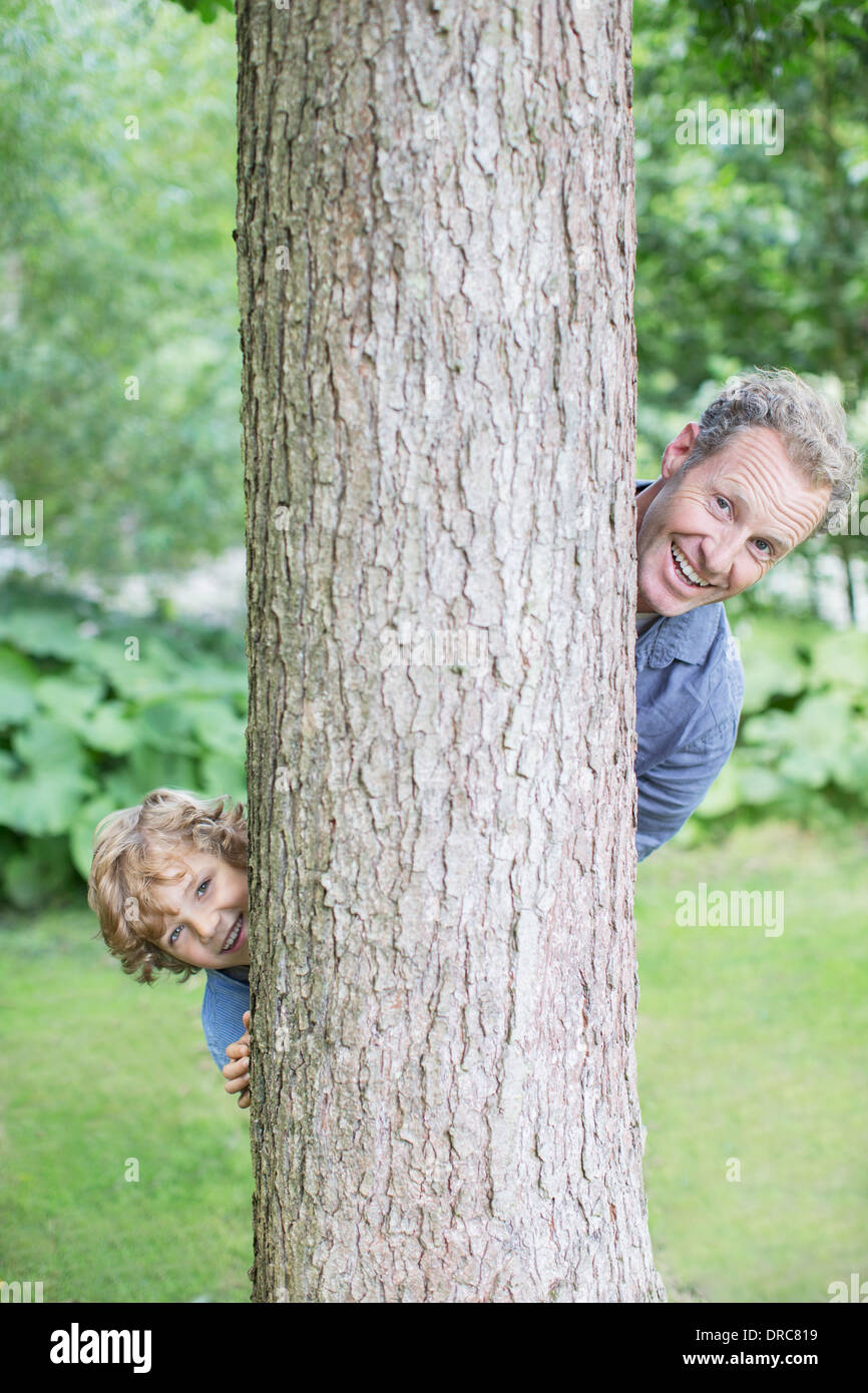 Father and son peering from behind tree Stock Photo