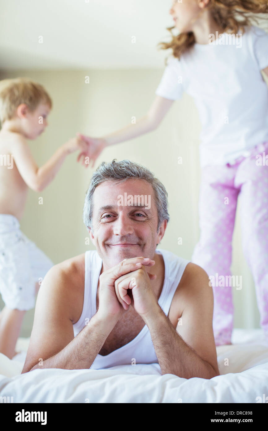 Children jumping on bed around father Stock Photo