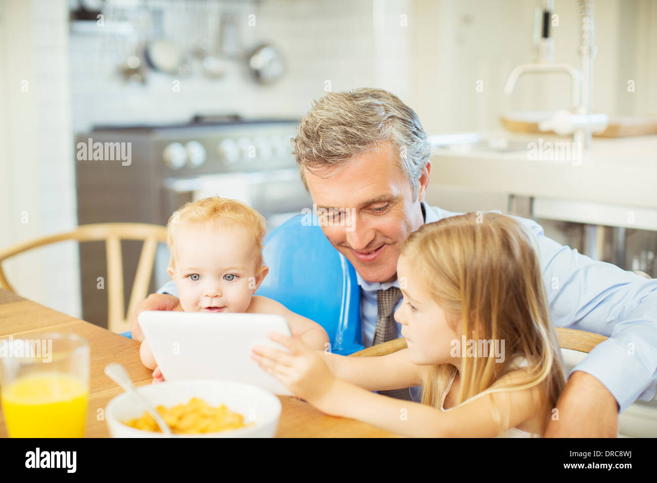 Father and children using digital tablet at table Stock Photo