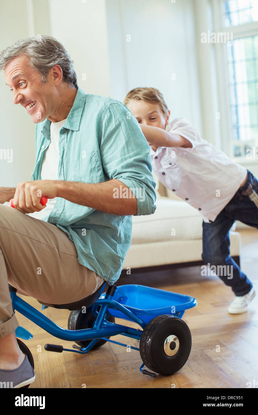Boy pushing father on tricycle indoors Stock Photo