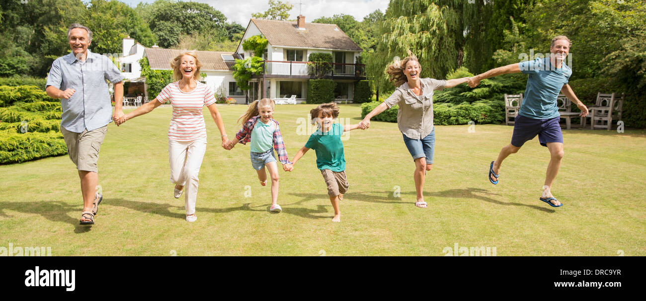Multi-generation family holding hands and running in grass Stock Photo