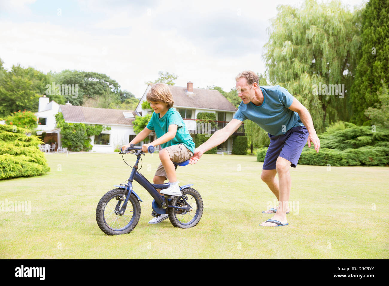 Father pushing son on bicycle in backyard Stock Photo