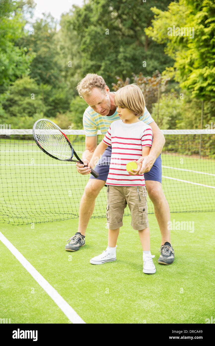 Father teaching son to play tennis on grass court Stock Photo