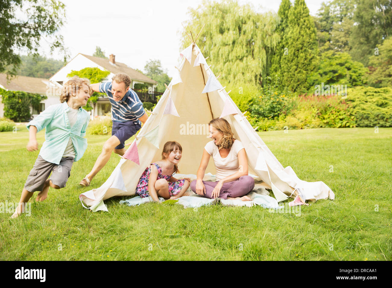 Father chasing son around teepee in backyard Stock Photo