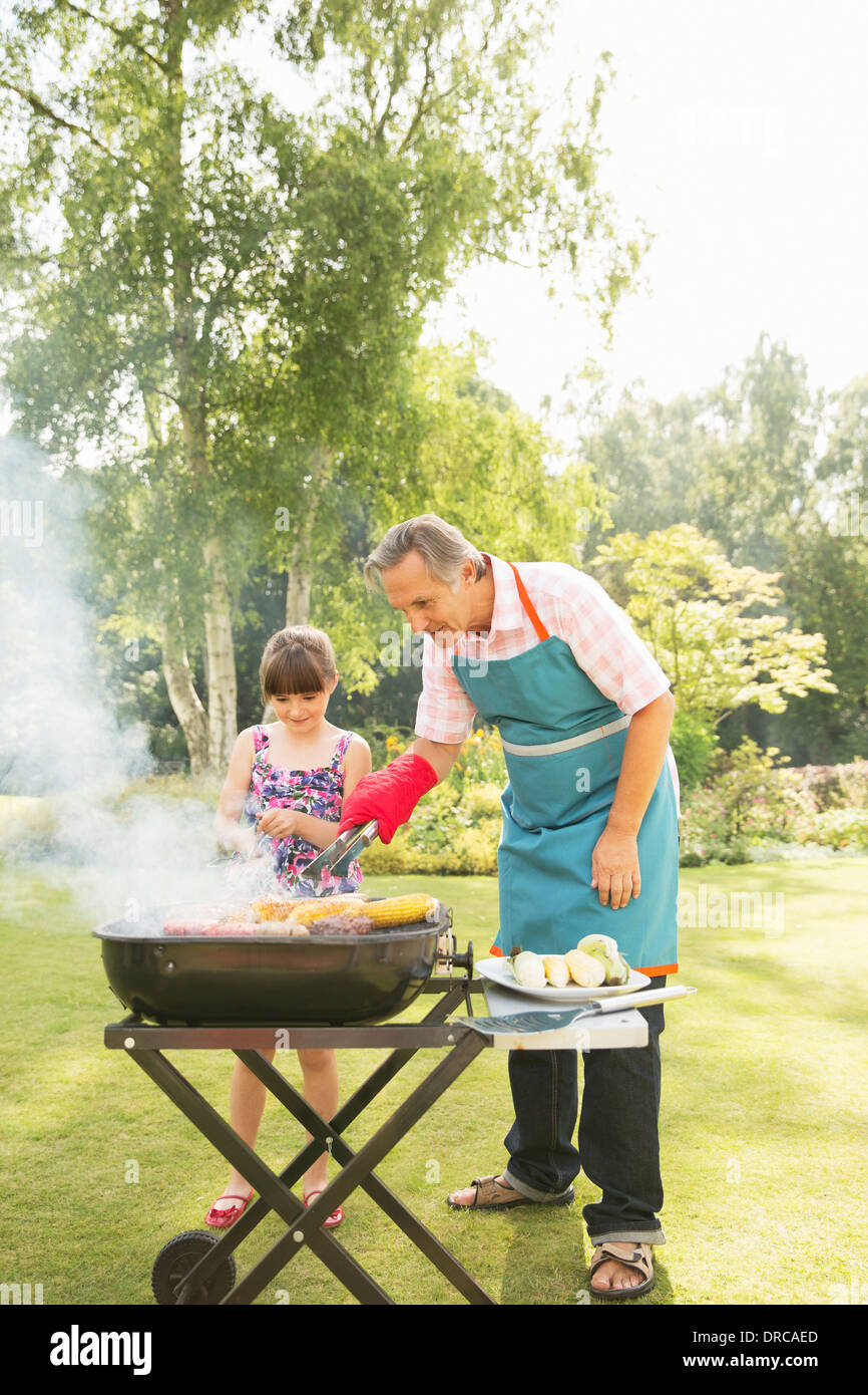 Grandfather and granddaughter grilling at barbecue in backyard Stock Photo