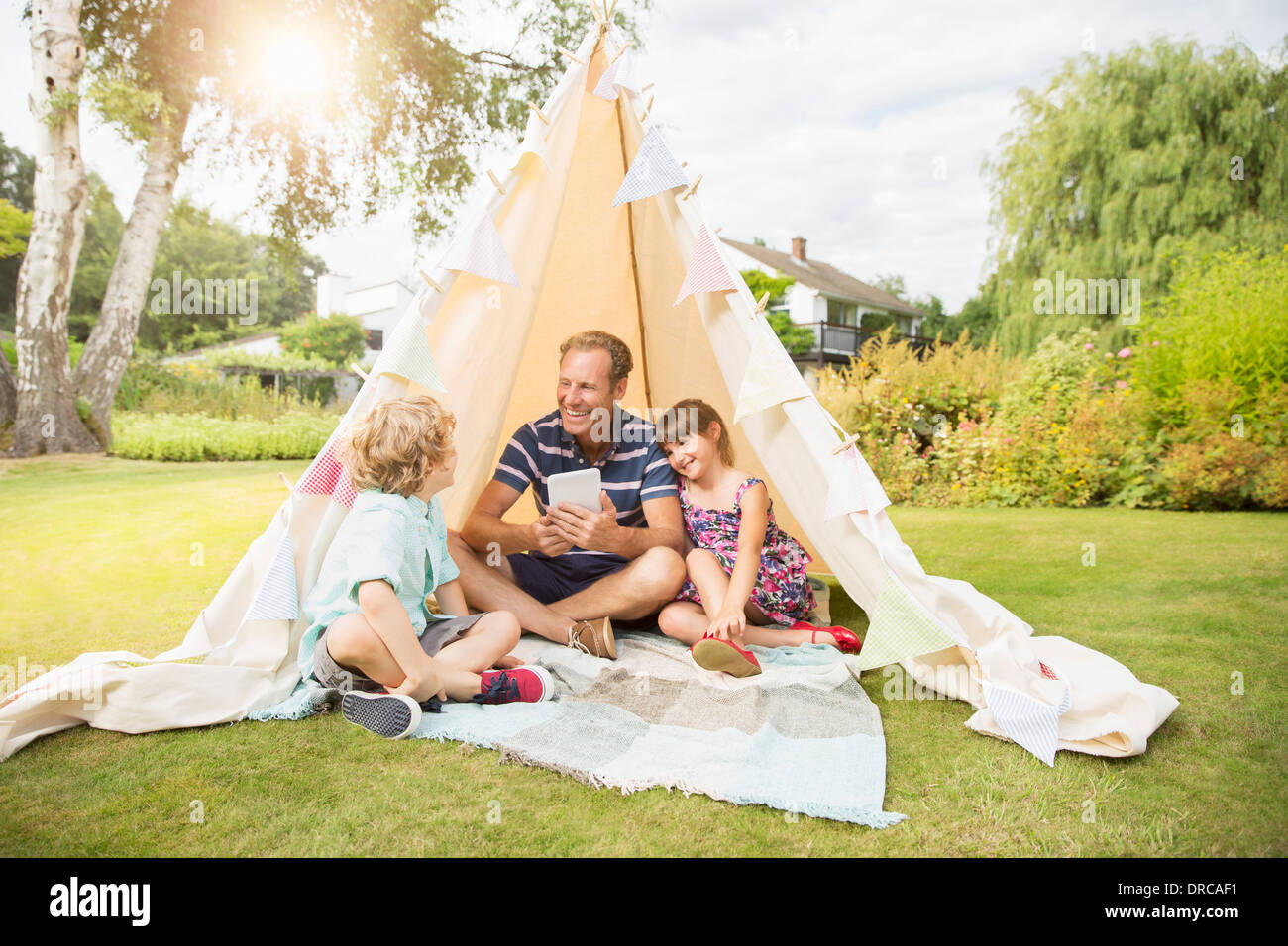 Father and children relaxing in teepee in backyard Stock Photo