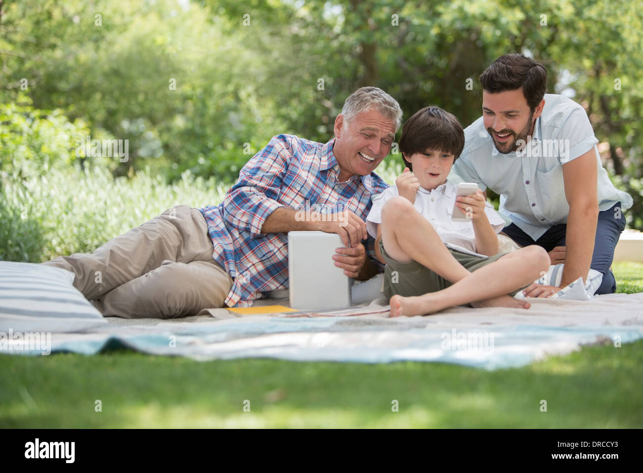 Multi-generation men with cell phone on blanket in grass Stock Photo