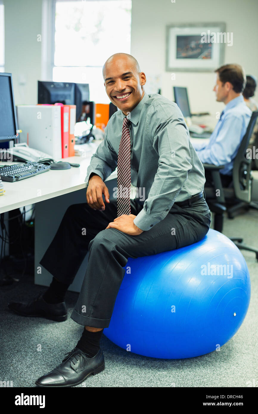 Businessman Sitting On Fitness Ball In Office Stock Photo