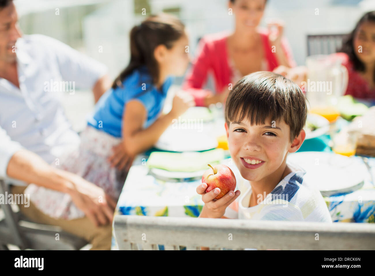 Boy eating fruit with family at table on sunny patio Stock Photo