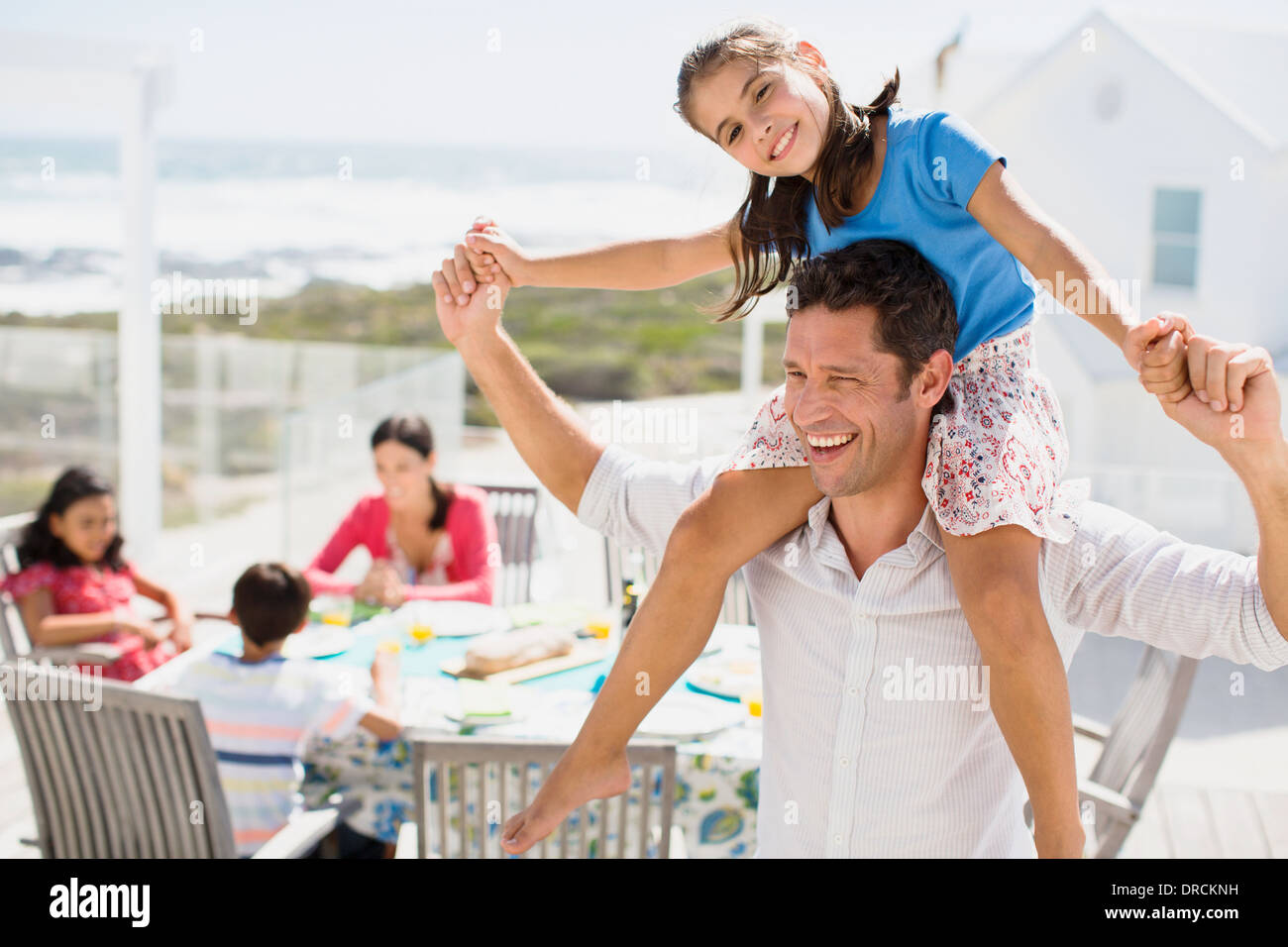 Father carrying daughter on shoulders on sunny patio Stock Photo