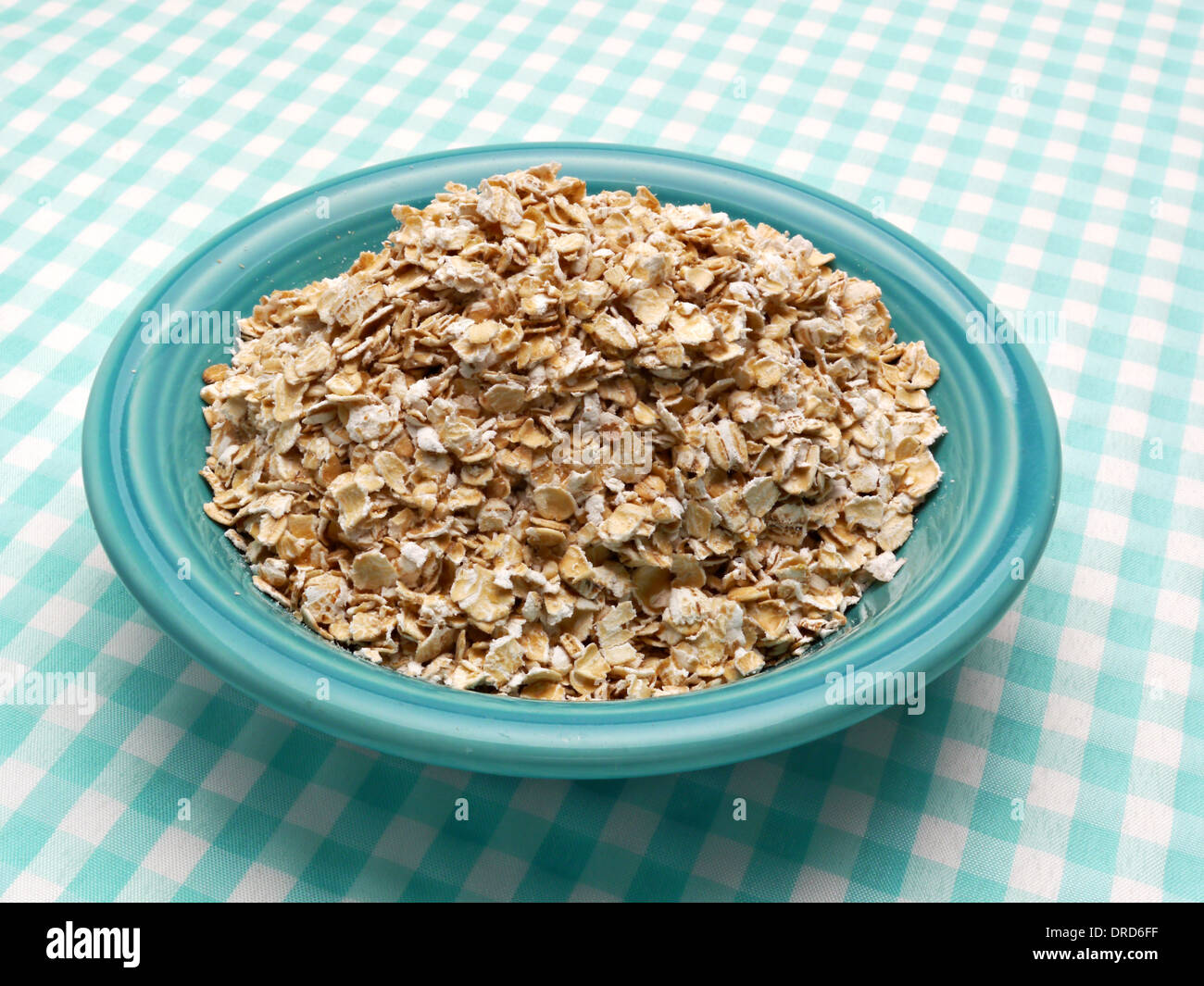 Uncooked oatmeal is sitting in a blue bowl on a blue and white checked table cloth. Stock Photo