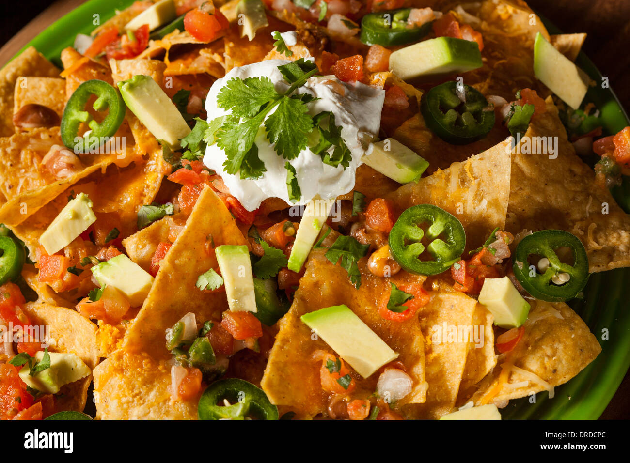 Homemade Unhealthy Nachos with Cheese, Sour Cream, and Vegetables Stock