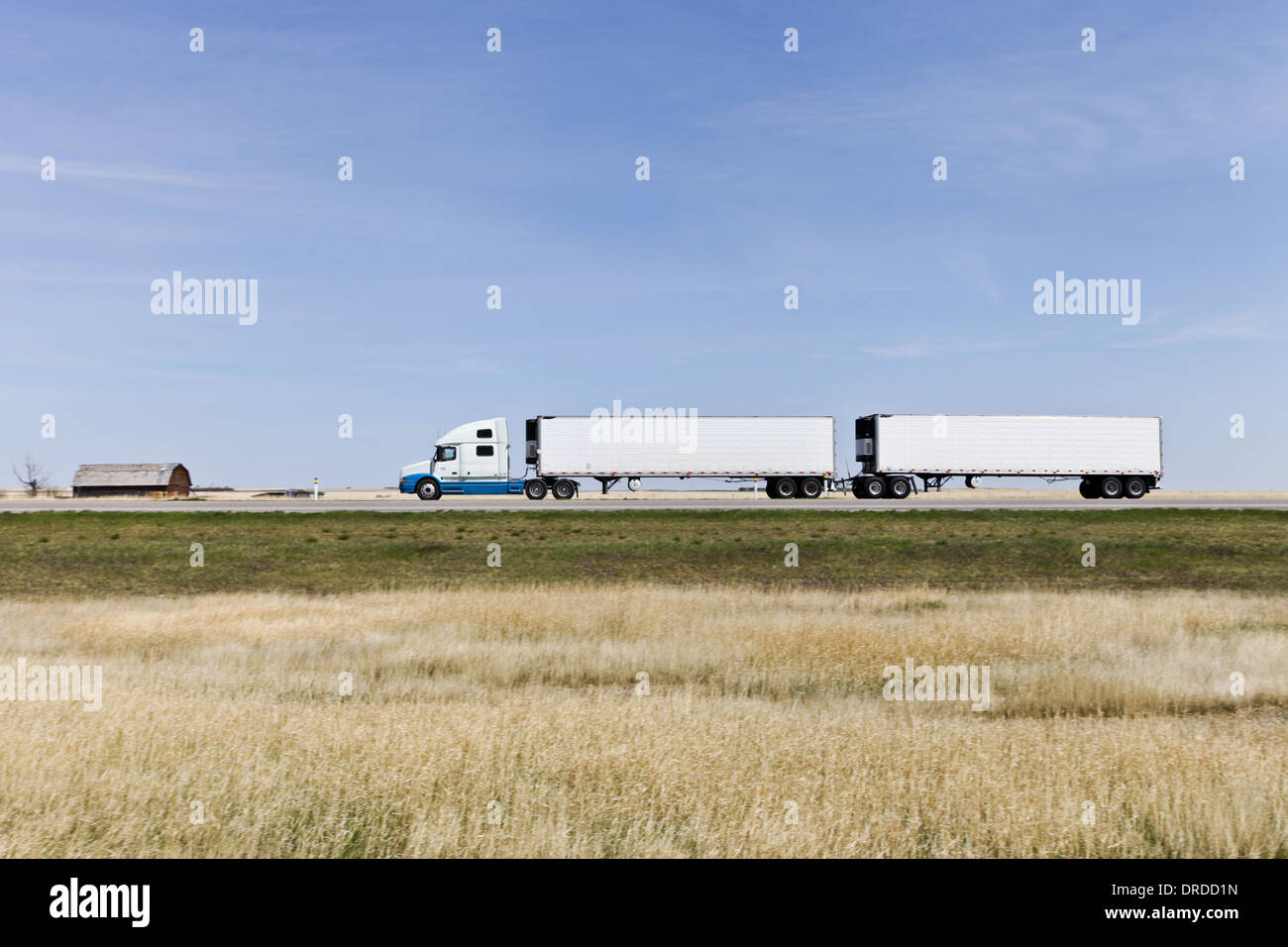 White Semi truck on the Highway heading right to left with motion blur of background two white reefer van trailers in turnpike double configuration Stock Photo