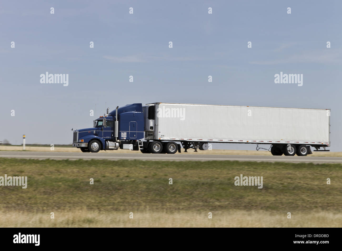 Blue Semi truck on the Highway heading right to left with motion blur of background, white box van twin axle trailer Stock Photo
