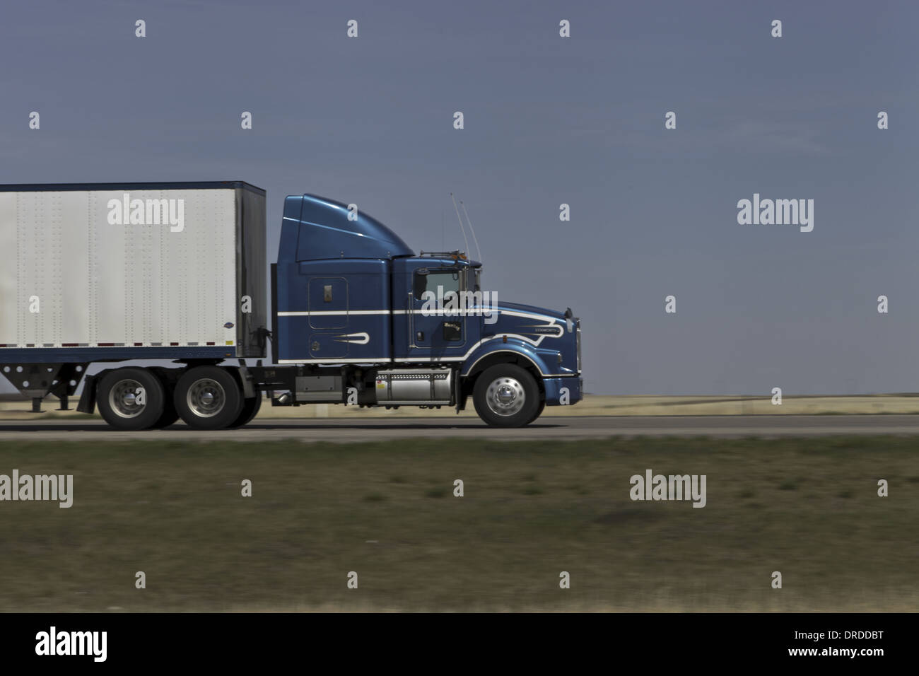 Blue Semi truck on the Highway heading left to right with motion blur of background, white box van trailer Stock Photo