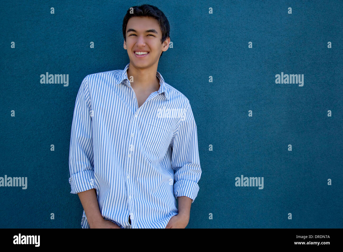 Teenage boy standing in front of a blue wall Stock Photo - Alamy