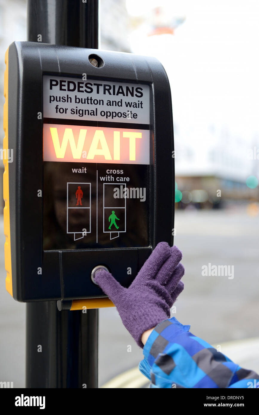 a young child pressing button at a road crossing aware of road safety focus on sign Stock Photo