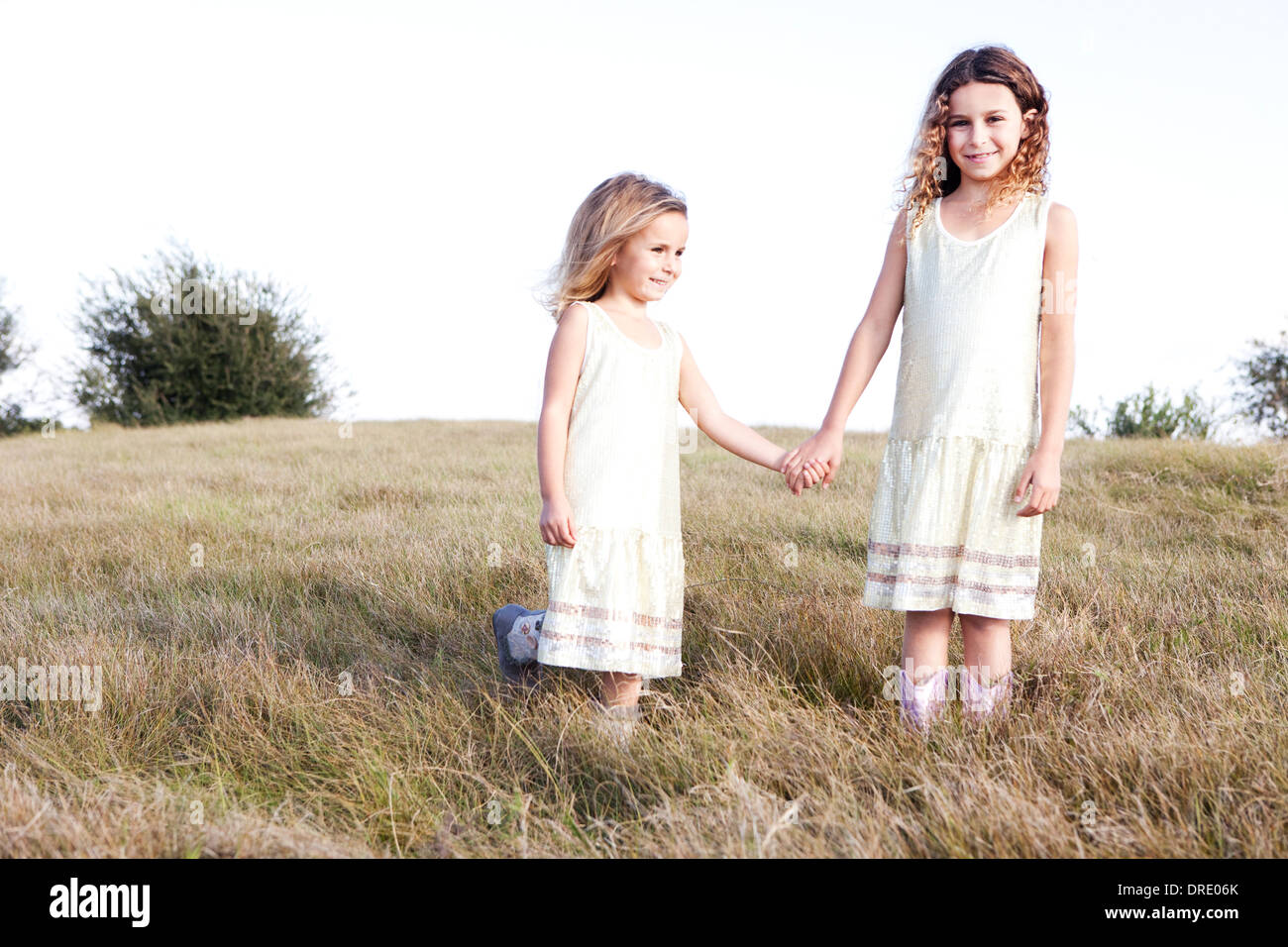 Sisters in dresses standing in field Stock Photo