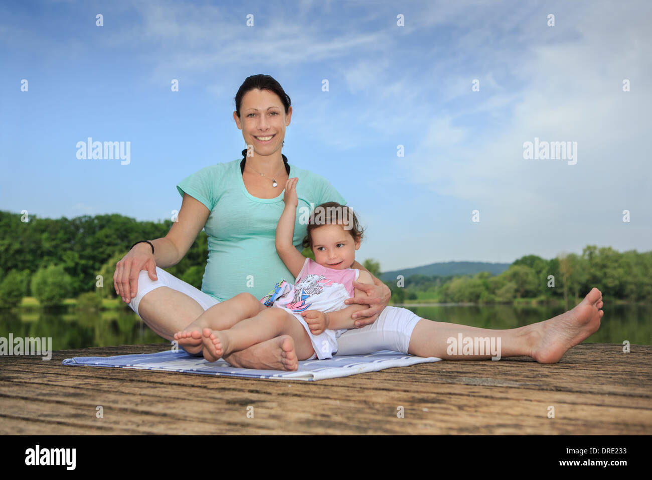 pregnant woman and her little daughter making yoga exercise at a lake Stock Photo