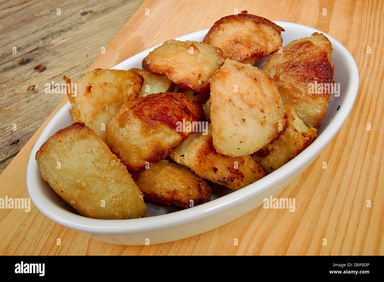 Crispy Roast potatoes in a serving dish against a traditional rustic kitchen table Stock Photo