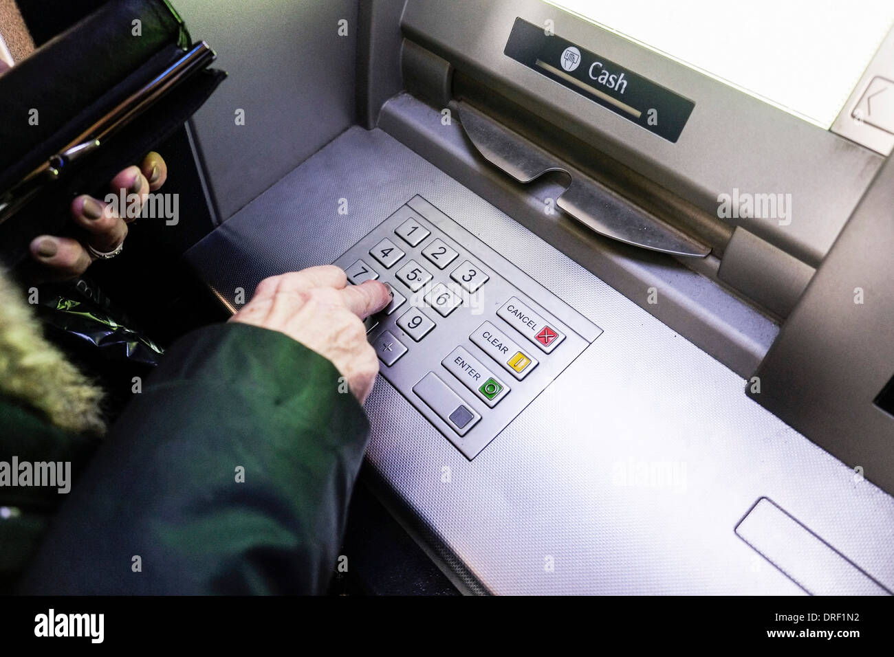 A woman keying her PIN into an ATM. Stock Photo
