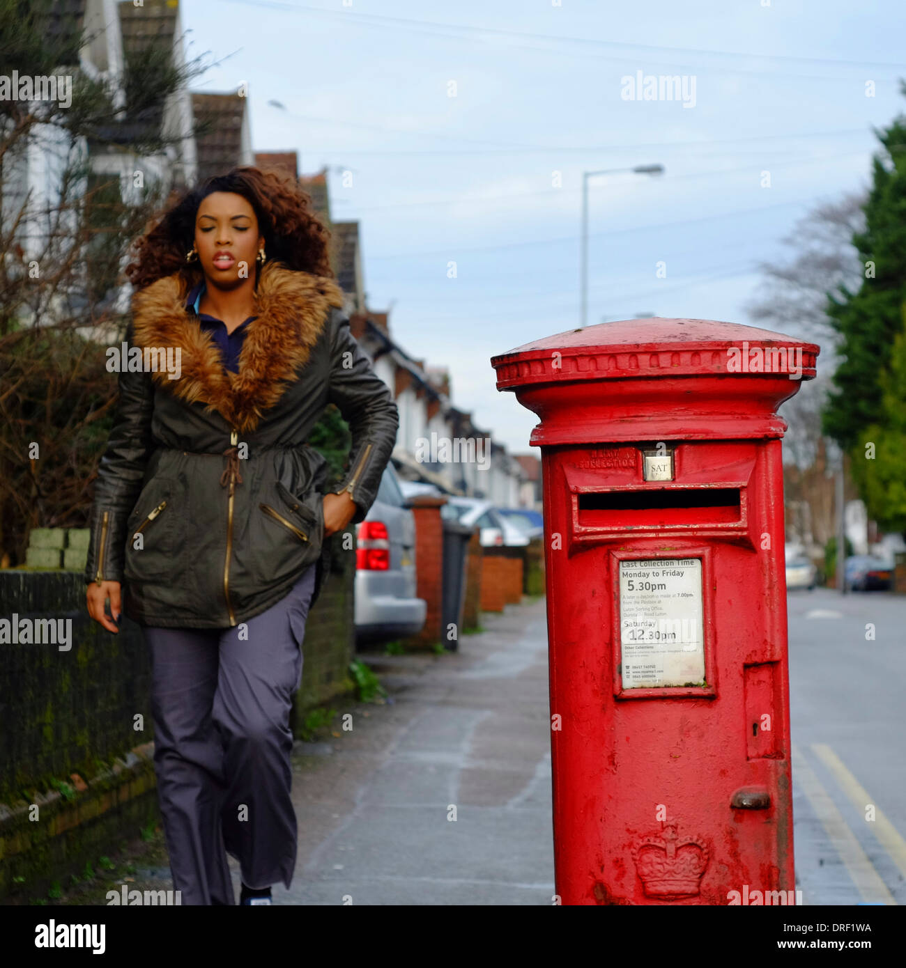 Attractive Black woman walking past red post box Stock Photo