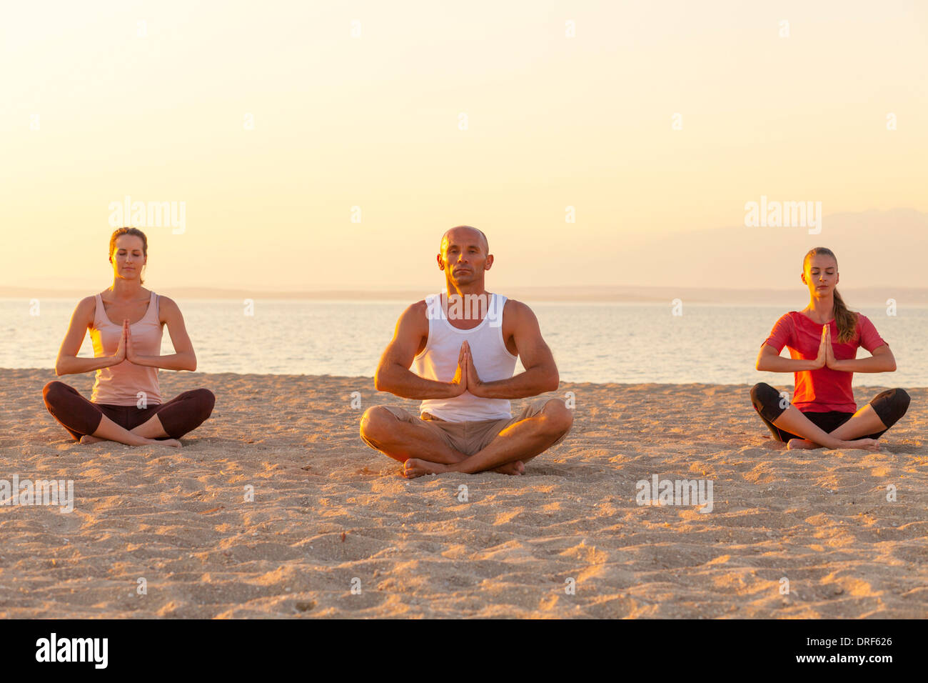 People practising yoga on beach, lotus pose Stock Photo - Alamy