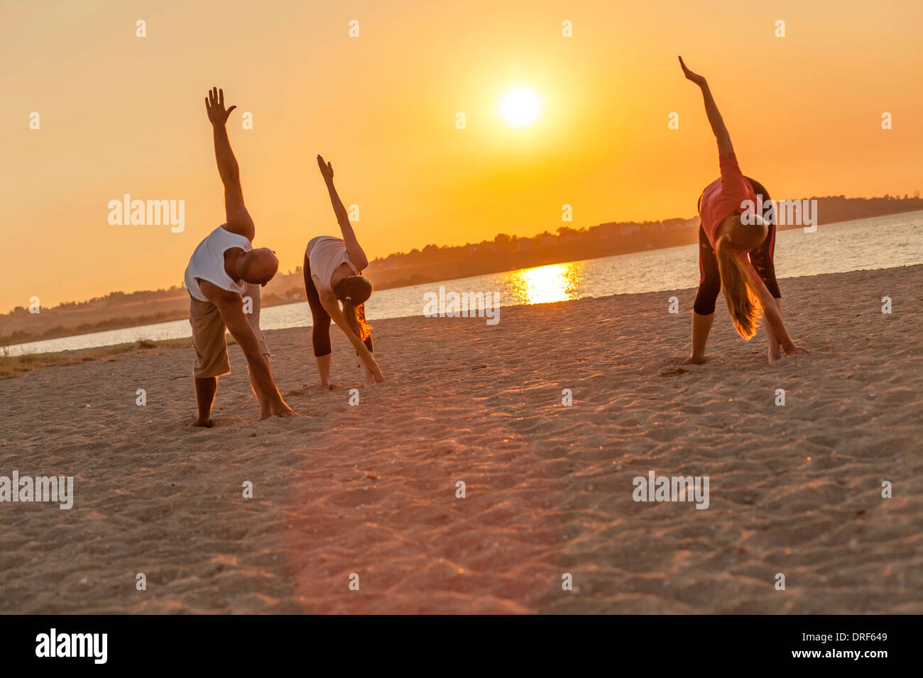 People practising yoga on beach, bending over Stock Photo