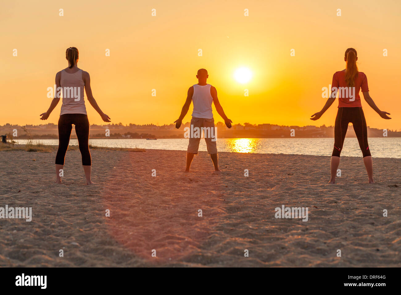 People practising yoga on beach, doing sun salutation Stock Photo