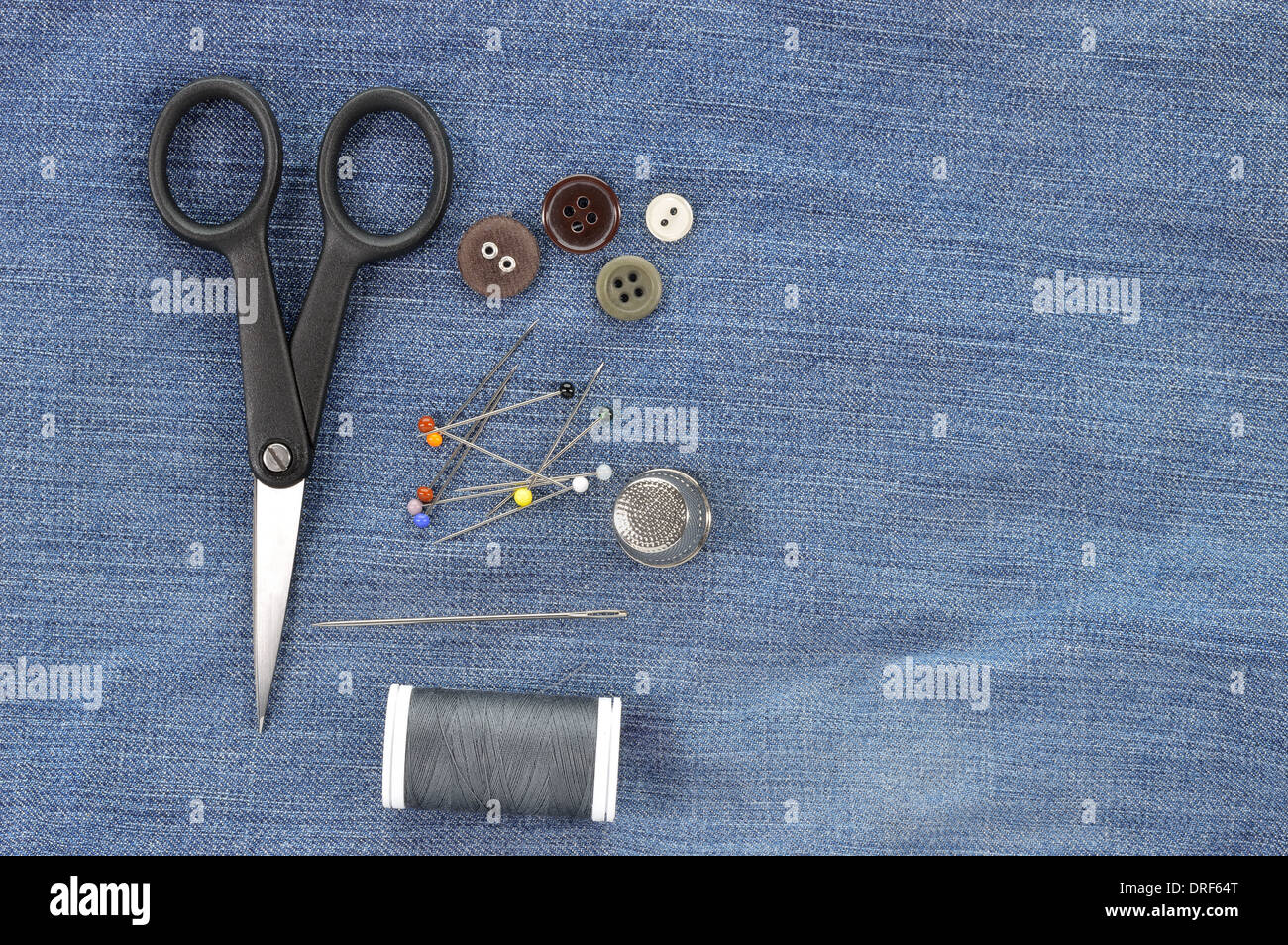 Sewing kit on jeans background. Needle, pins, buttons, thread, thimble and scissors - repair set. Copy space. Stock Photo