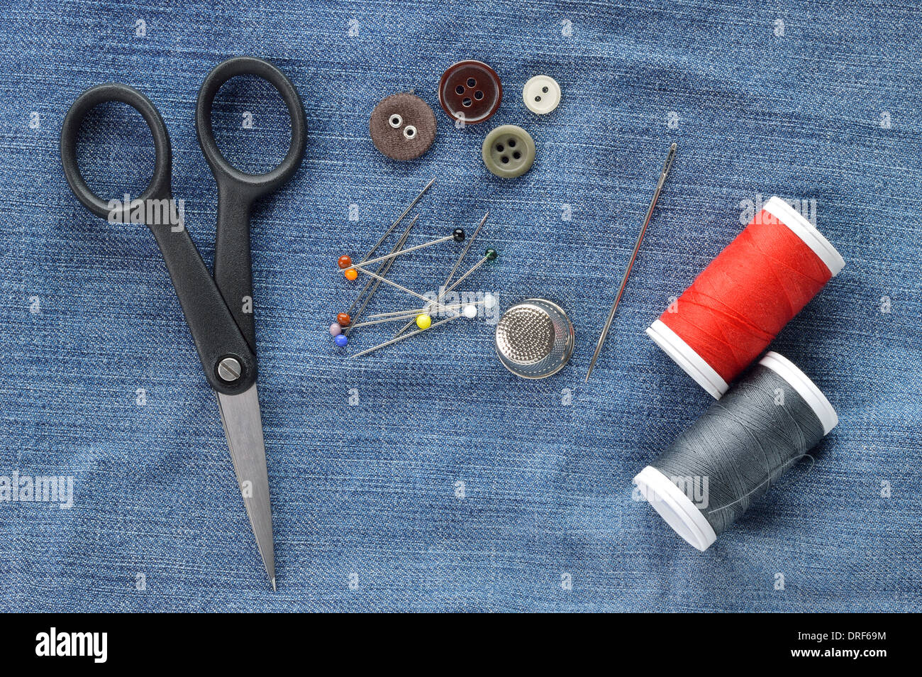 Sewing kit on jeans background. Needle, pins, buttons, thread, thimble and scissors - repair set. Stock Photo