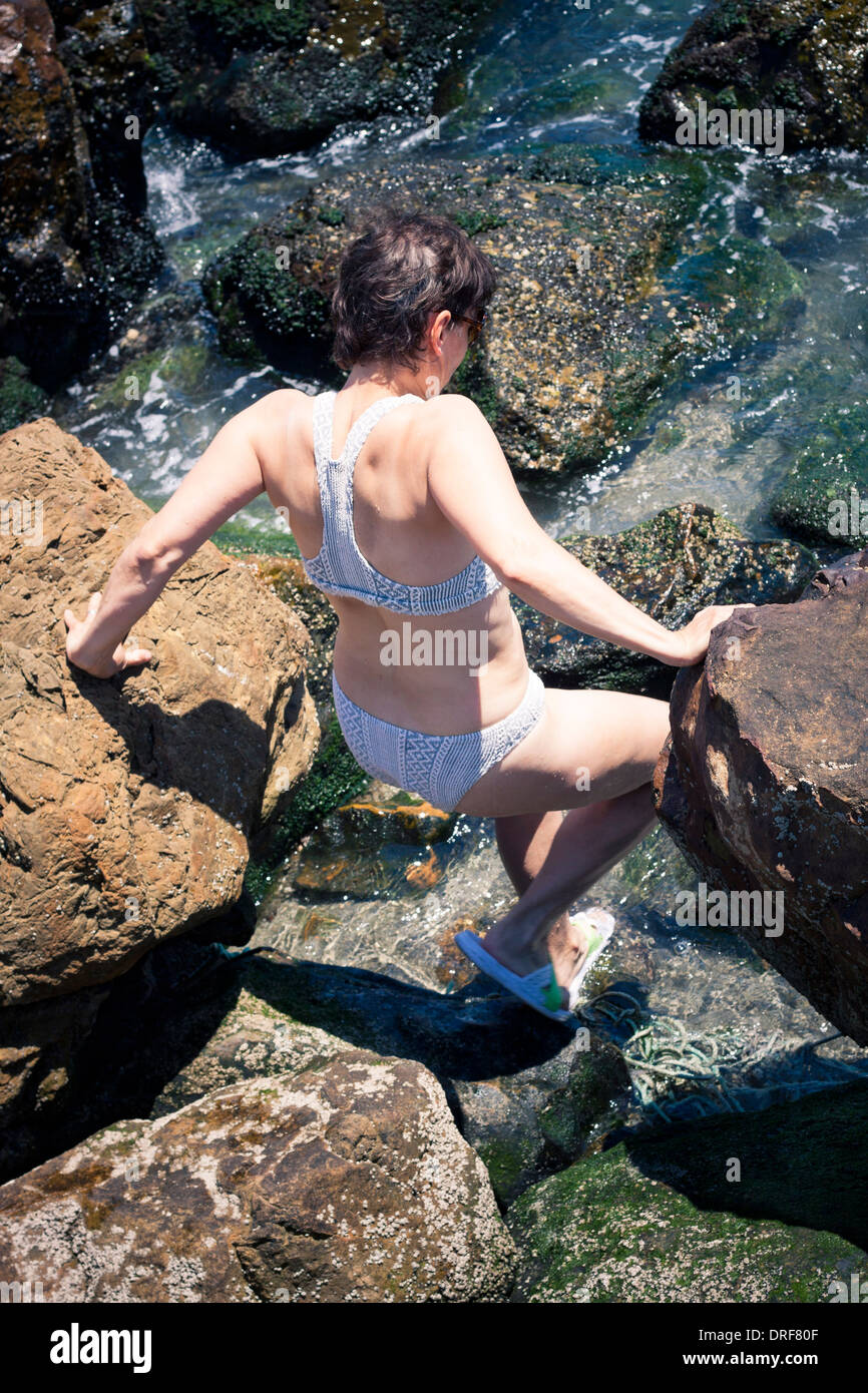 Middle aged woman walking in water on the rocky beach. Stock Photo