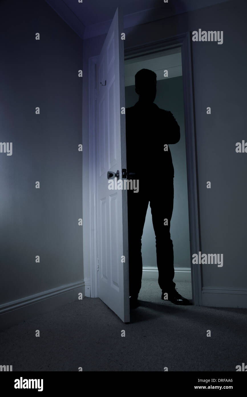 Silhouette of a man standing in the dark in an open doorway. Stock Photo
