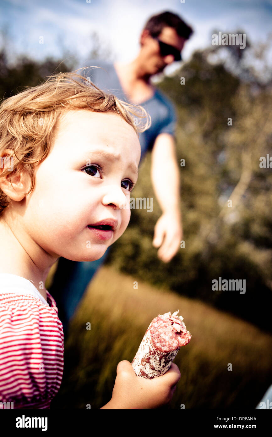 Little girl eating a sausage, man in background, Bavaria, Germany Stock