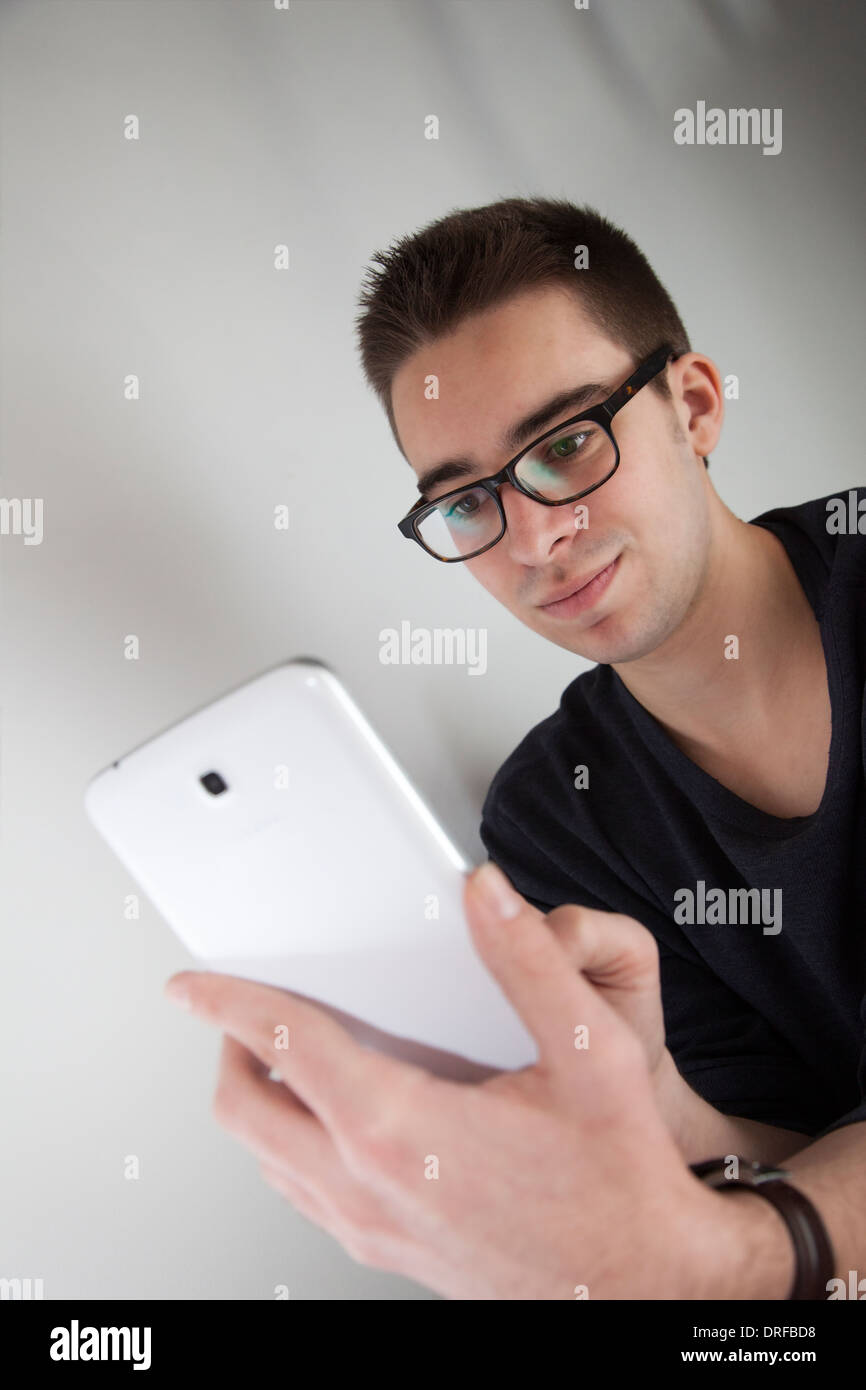 Good looking young man wearing glasses, holding a white digital tablet. Portrait shaped. Stock Photo