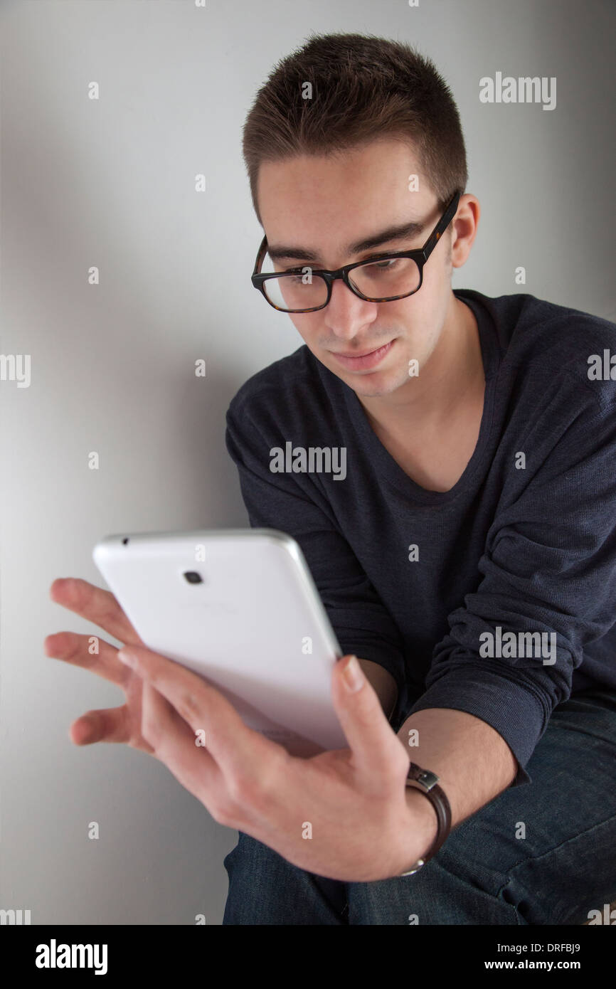 Good looking young man wearing glasses, holding a white digital tablet. Portrait shaped. Stock Photo