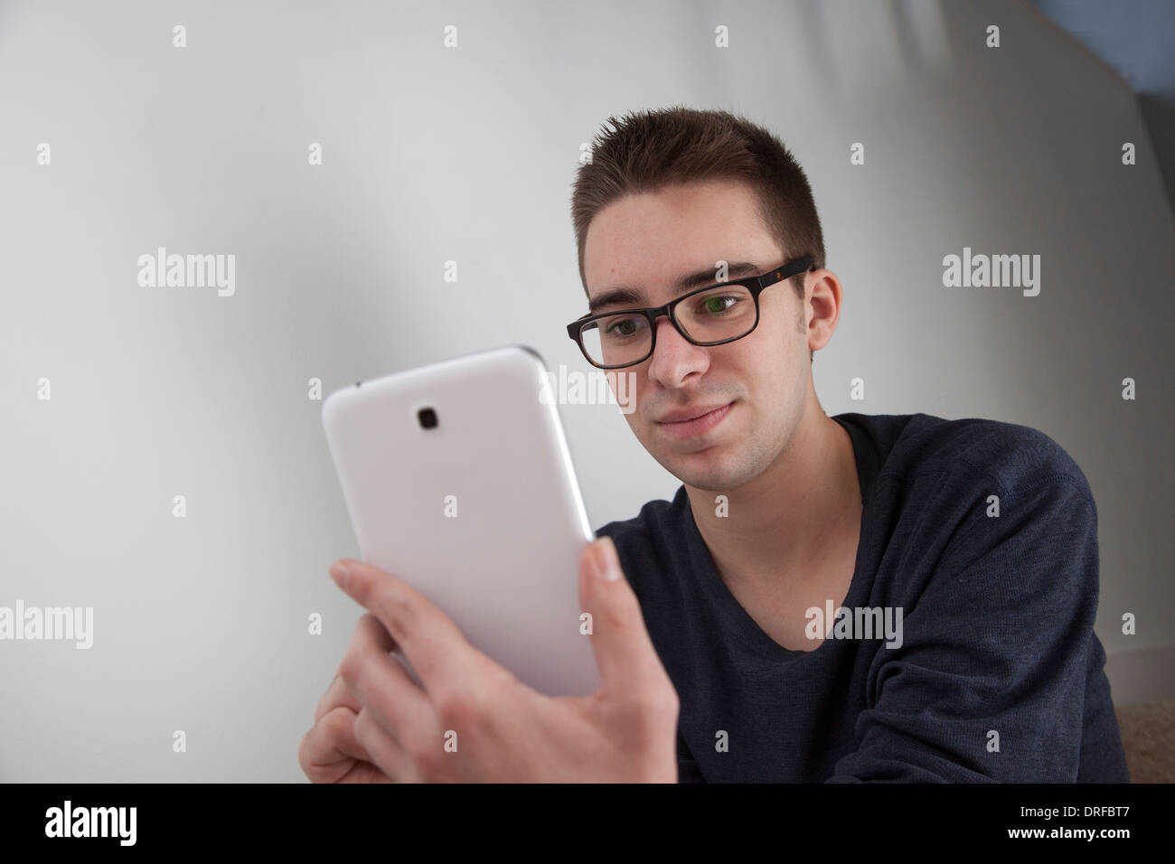 Good looking young man wearing glasses, holding a white digital tablet. Landscape shape, with copy space. Stock Photo