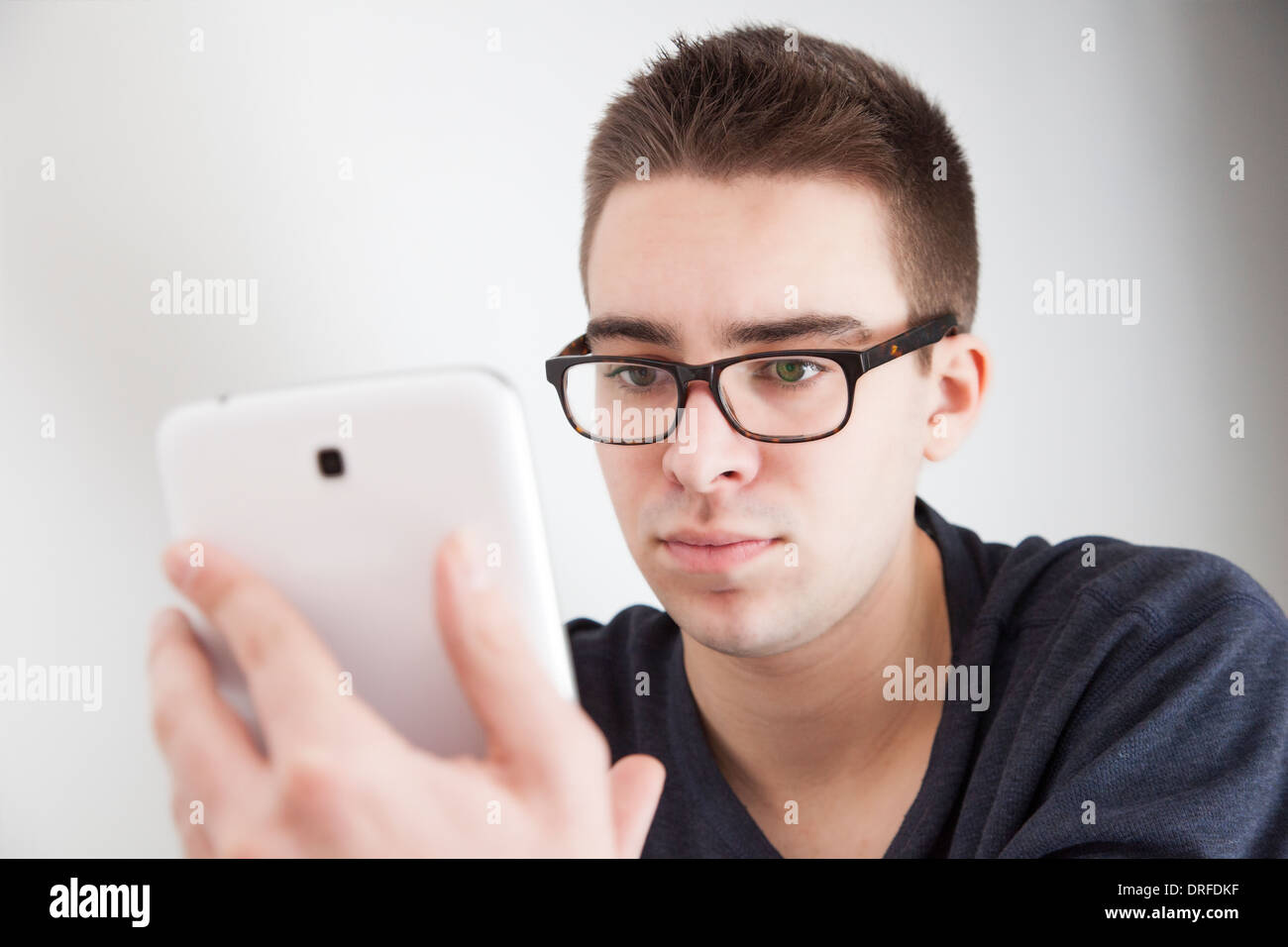 Good looking young man wearing glasses, holding a white digital tablet. Serious expression. Stock Photo