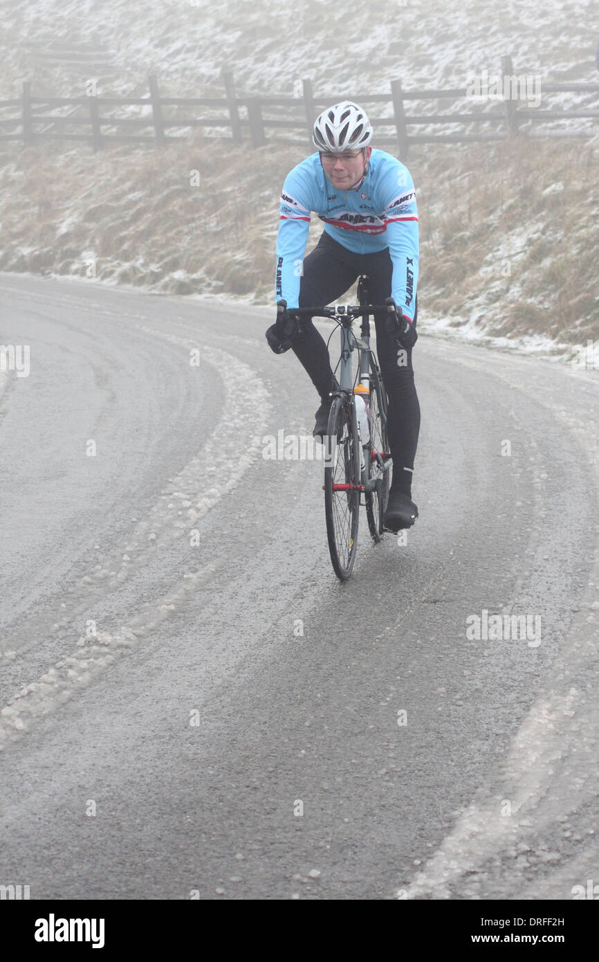 A cyclist tackles mist and snowy road conditions adjacent to Mam Tor in Castleton, Peak District National Park, England, UK Stock Photo